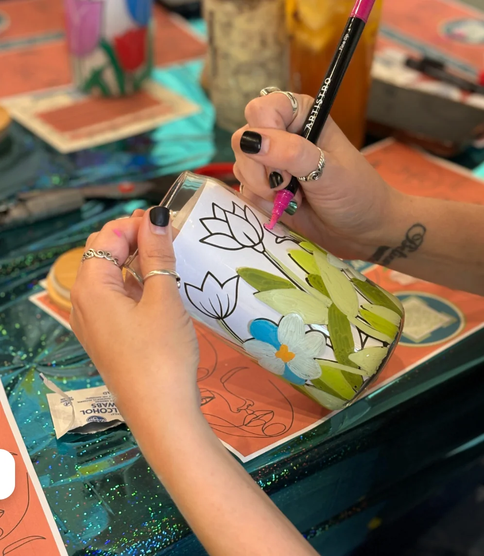 Person painting a floral design on a glass jar
