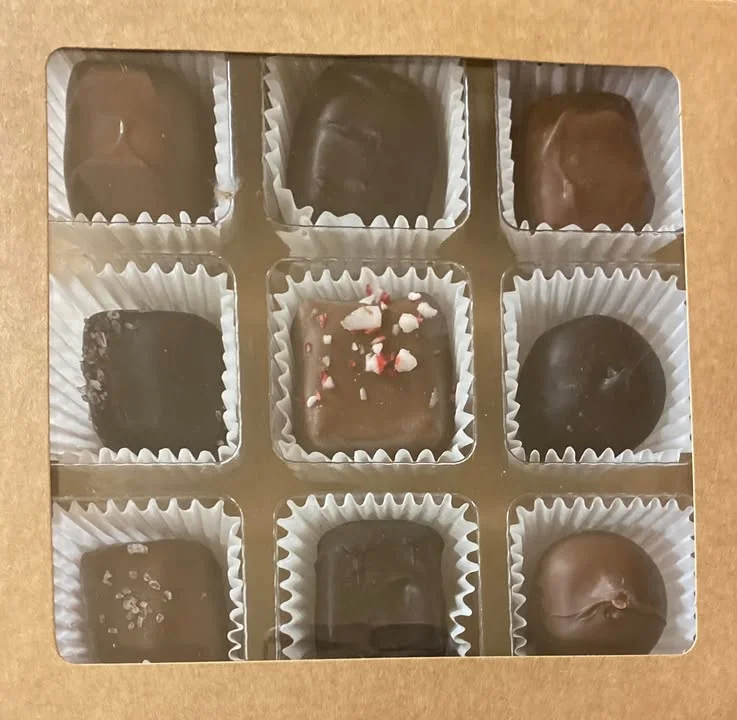 A box of assorted chocolates arranged in a grid, featuring a variety of toppings and flavors.