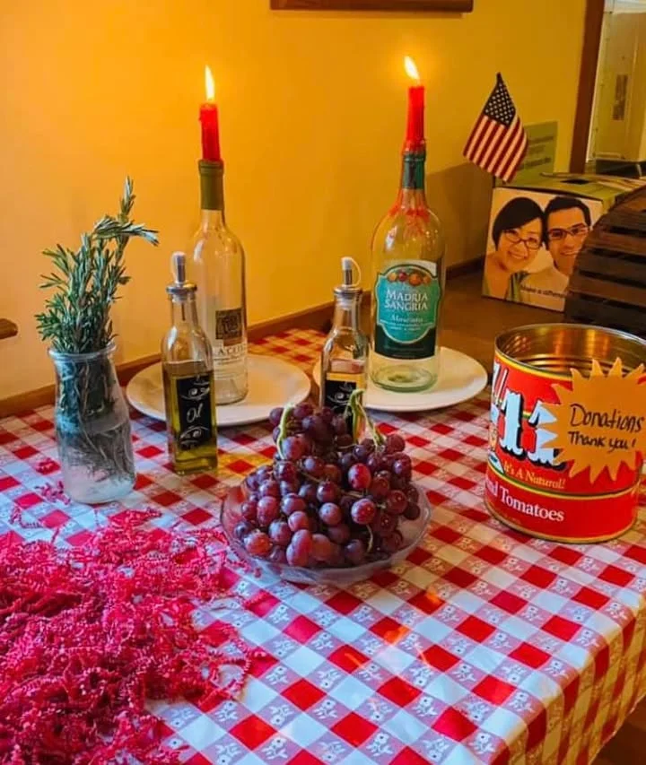A table set with candles, bottles of wine, and grapes, surrounded by a checkered tablecloth and decorations.