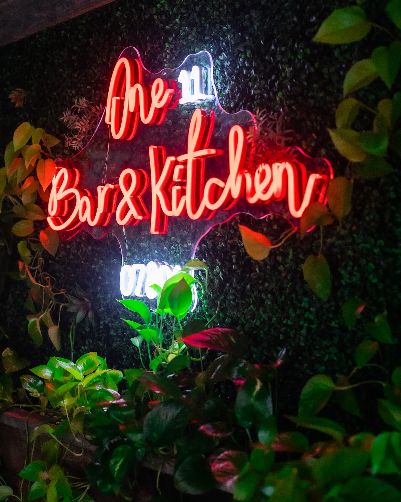 Neon sign of One 11 Bar & Kitchen surrounded by greenery