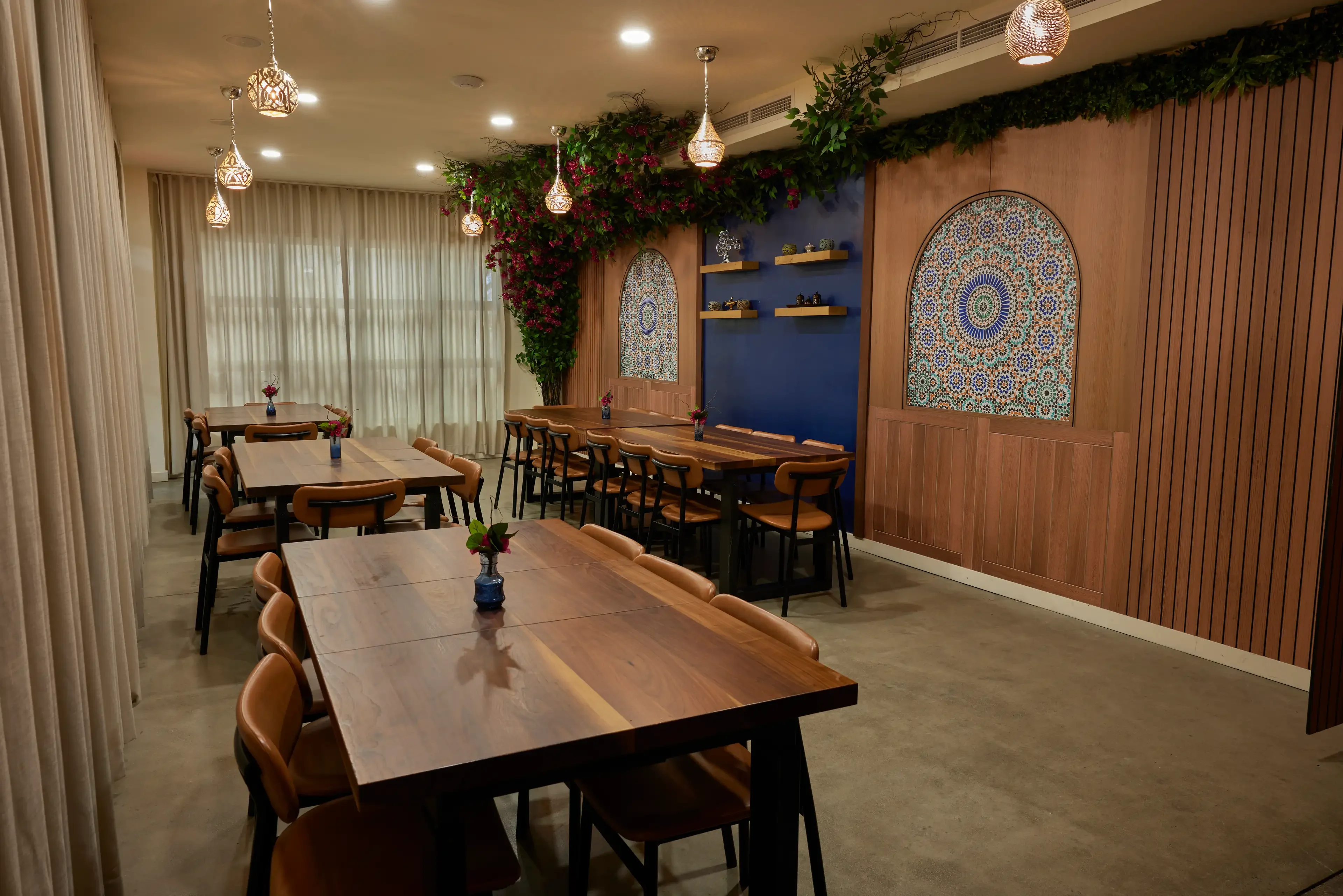 Chic and cozy dining room with wooden tables, warm lighting, and decorative tiles. Greenery and floral accents create a welcoming, elegant ambiance.