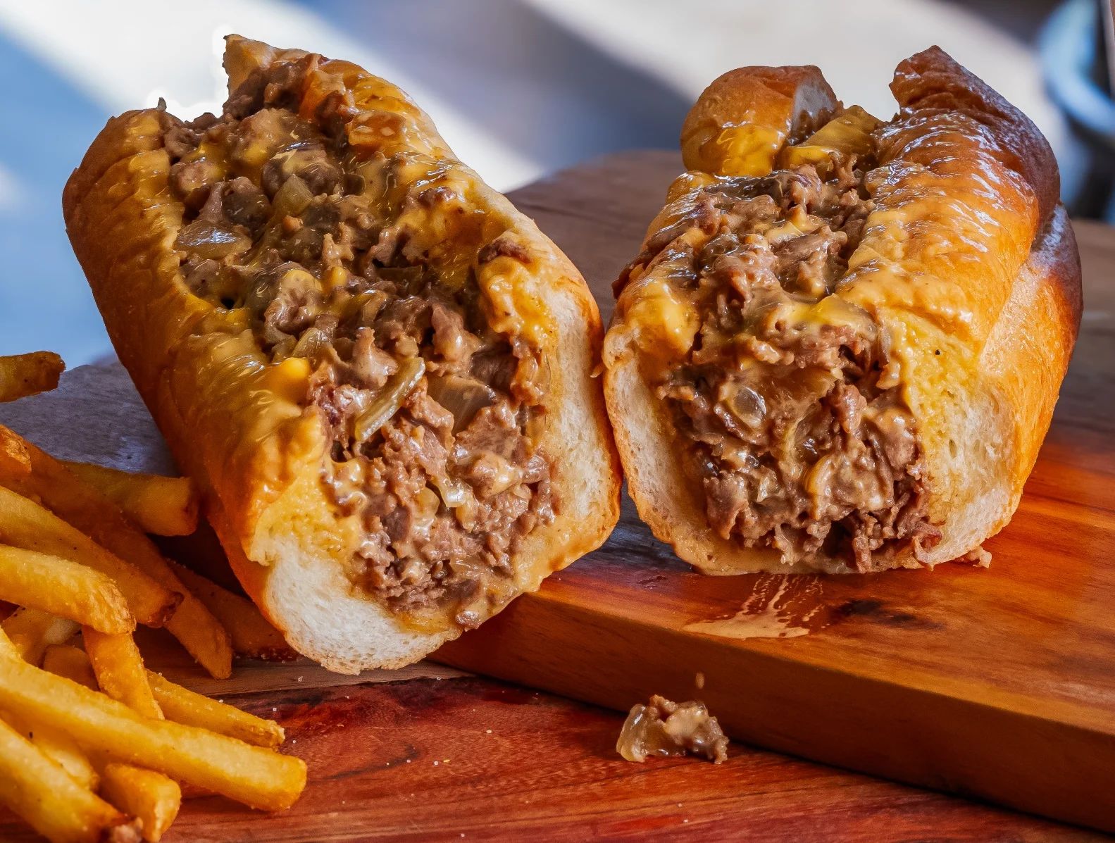 A hearty sub sandwich filled with beef, cheese, and vegetables, accompanied by a side of crispy French fries on parchment paper.