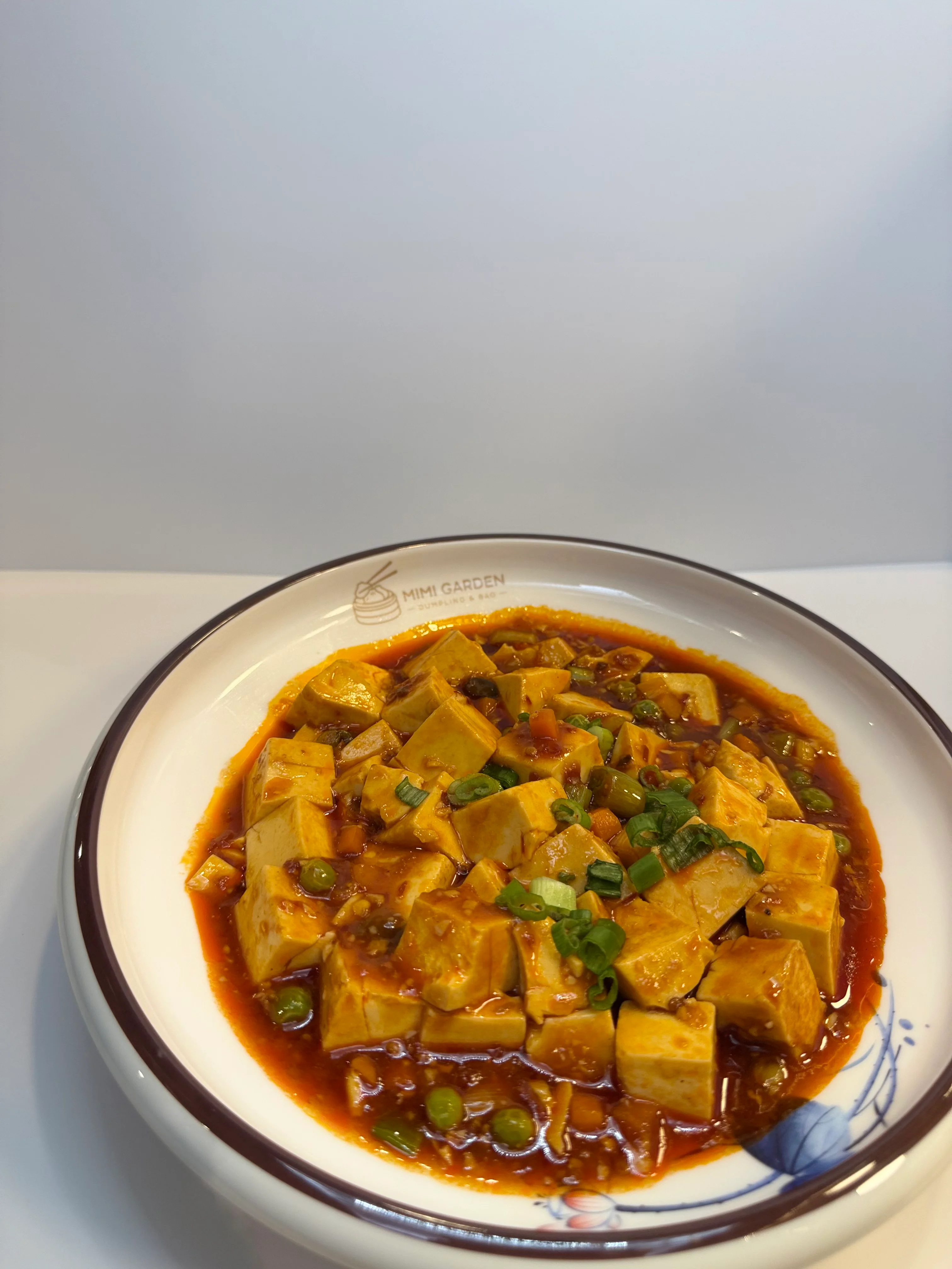 A bowl of stir-fried tofu cubes and vegetables, coated in a rich, spicy sauce, garnished with chopped green onions.
