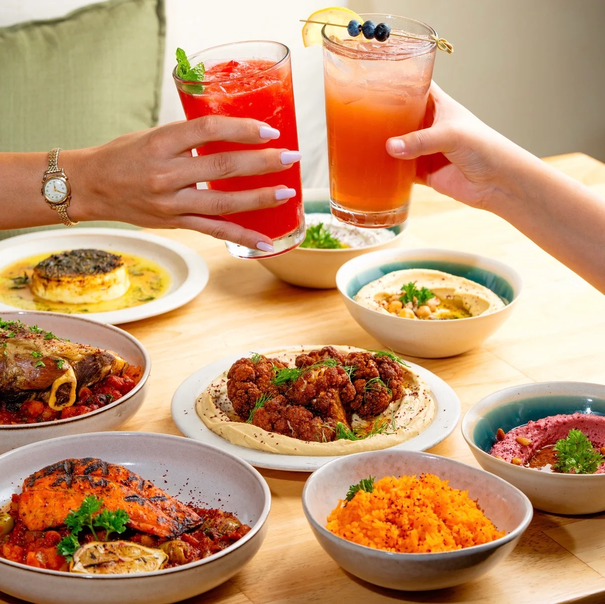 Colorful Mediterranean feast with cocktails and various dishes on a wooden table