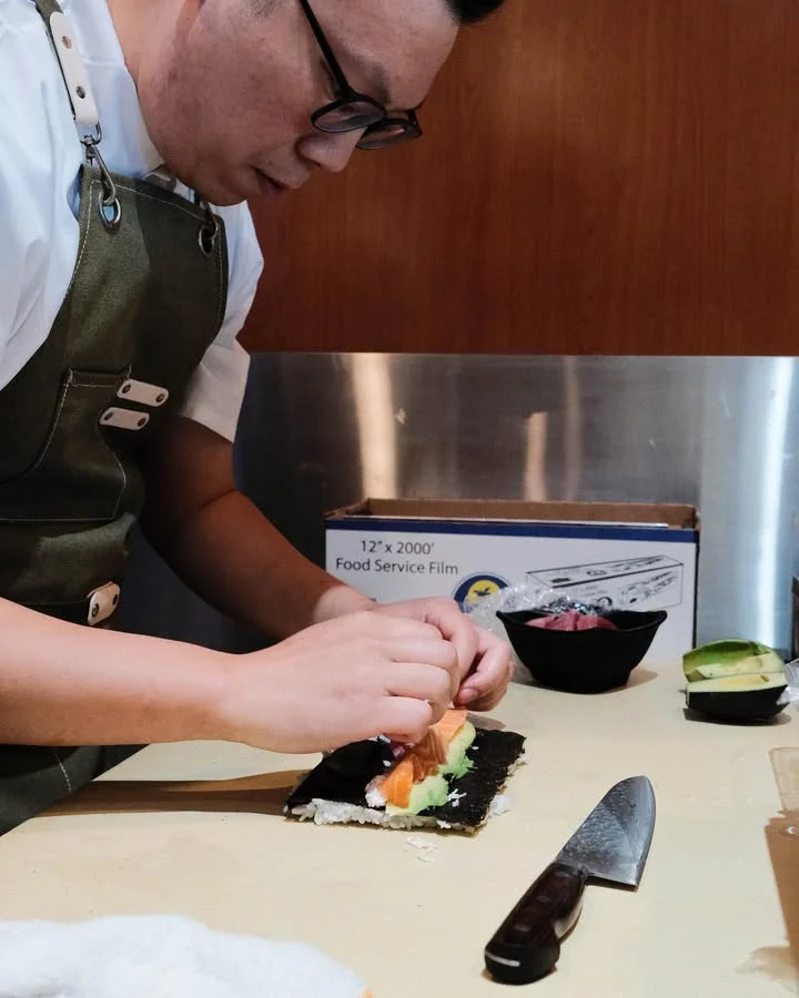 A chef skillfully assembling sushi with colorful ingredients on seaweed.