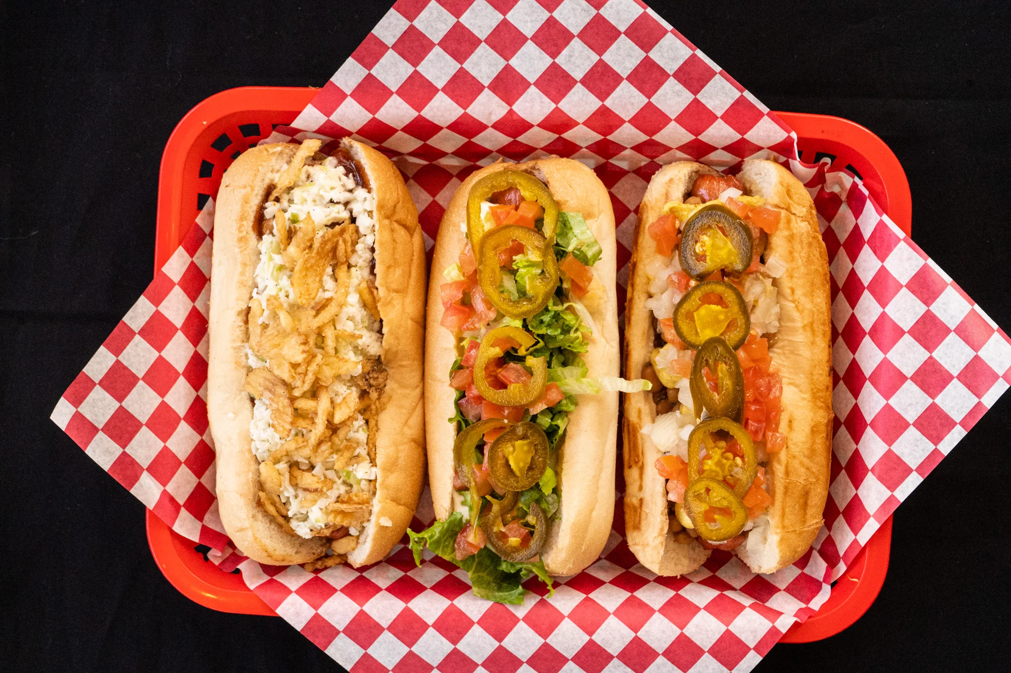 Three gourmet hot dogs with toppings in a red basket