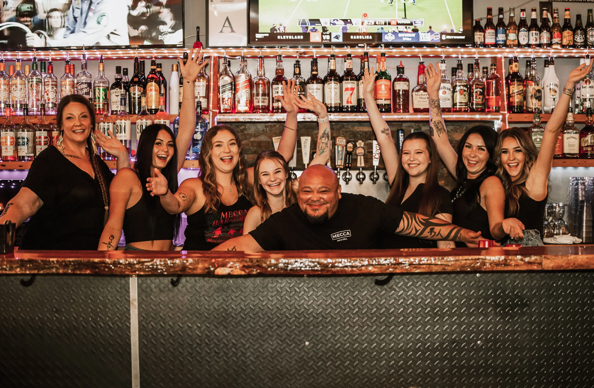 Cheerful bartenders posing behind a vibrant bar counter