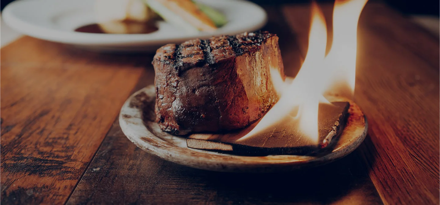 Flaming steak on a wooden plate, showcasing a dramatic presentation