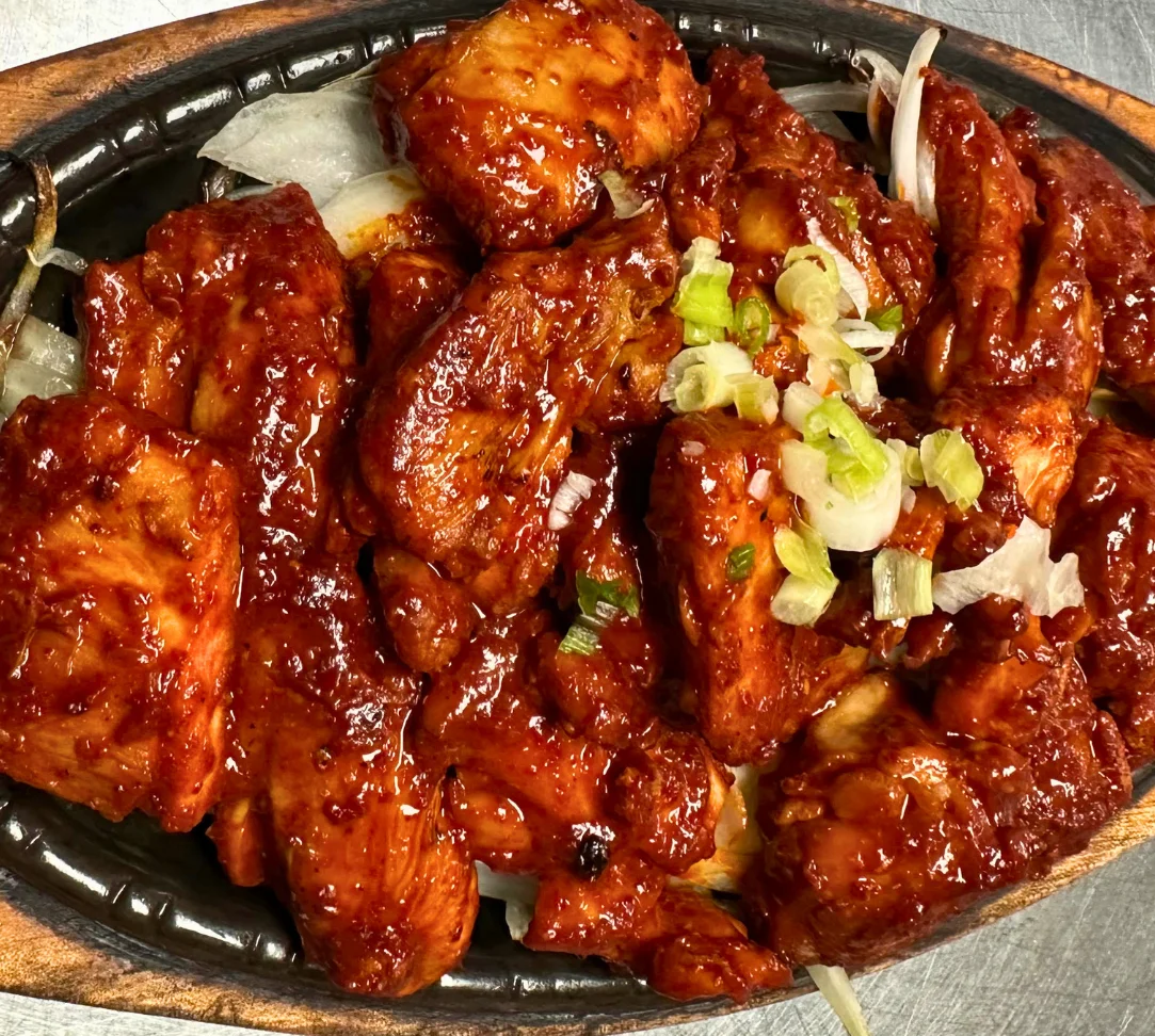 Sizzling beef dish topped with green onions on a black plate.