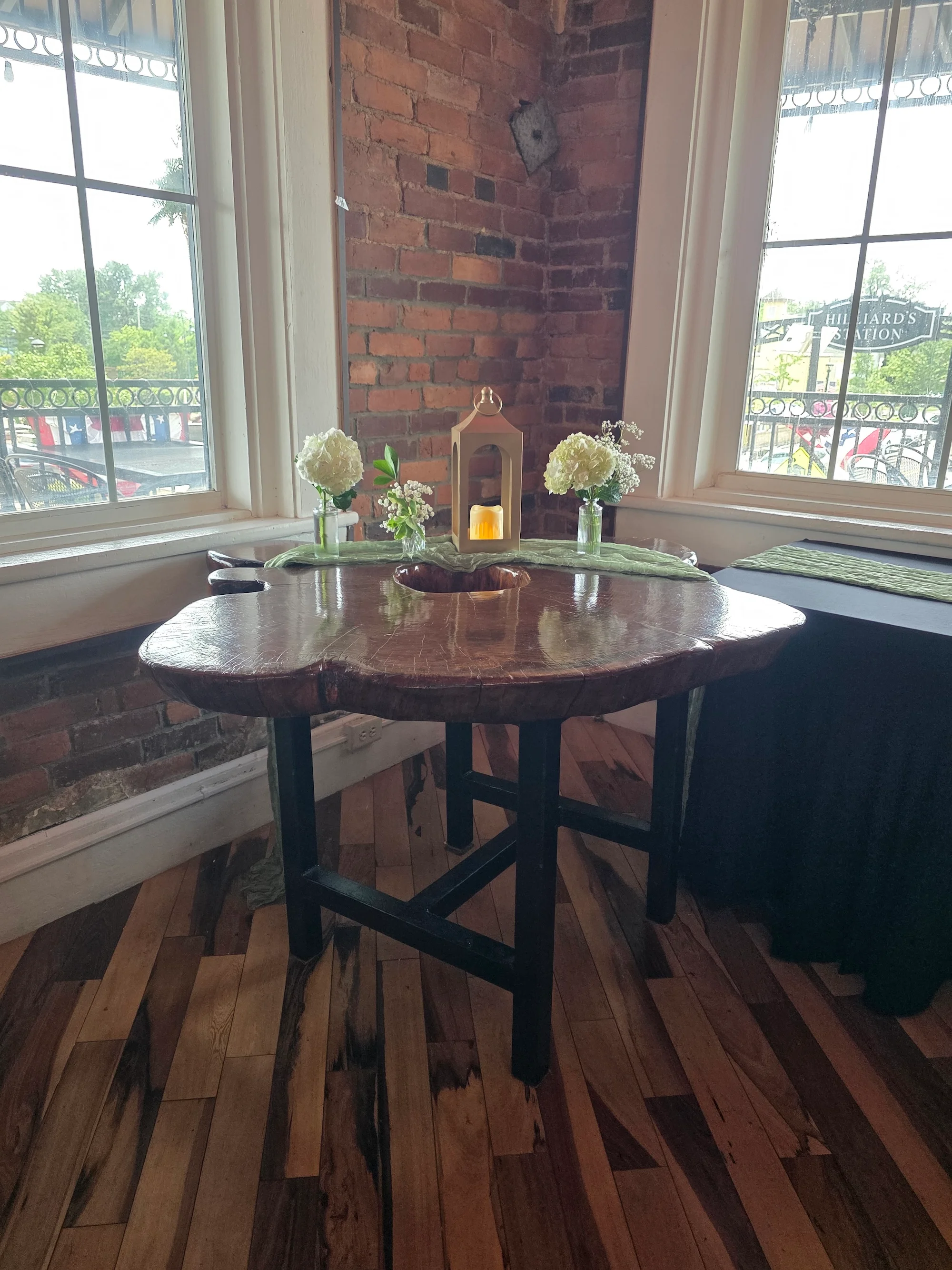 A rustic table set with flowers and a candle, positioned near a window with a view.