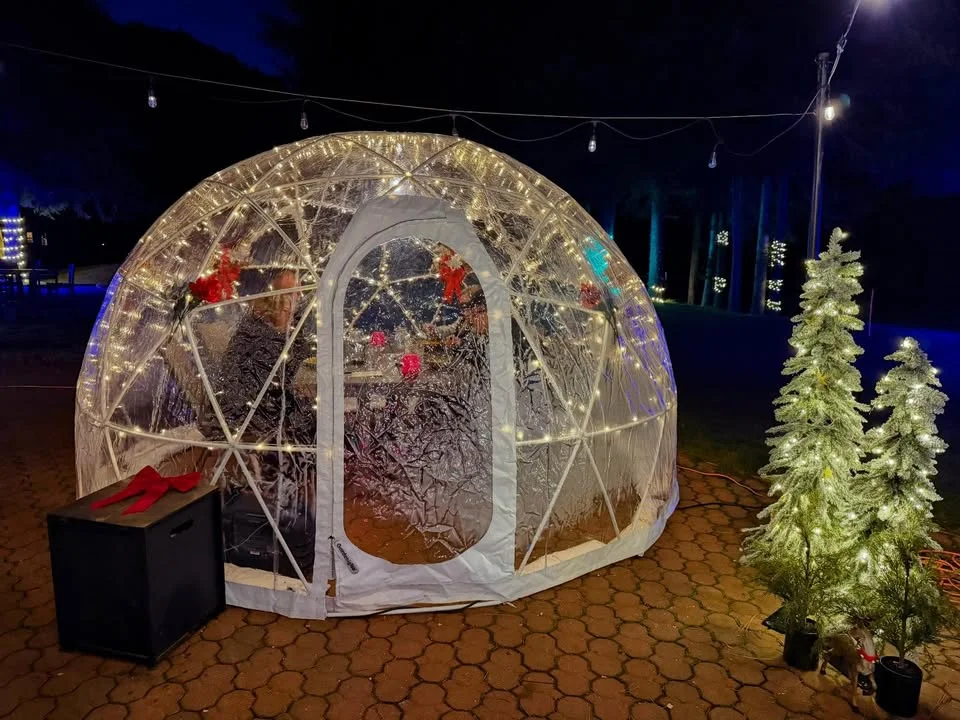 A beautifully lit outdoor igloo structure at night, surrounded by decorative trees.