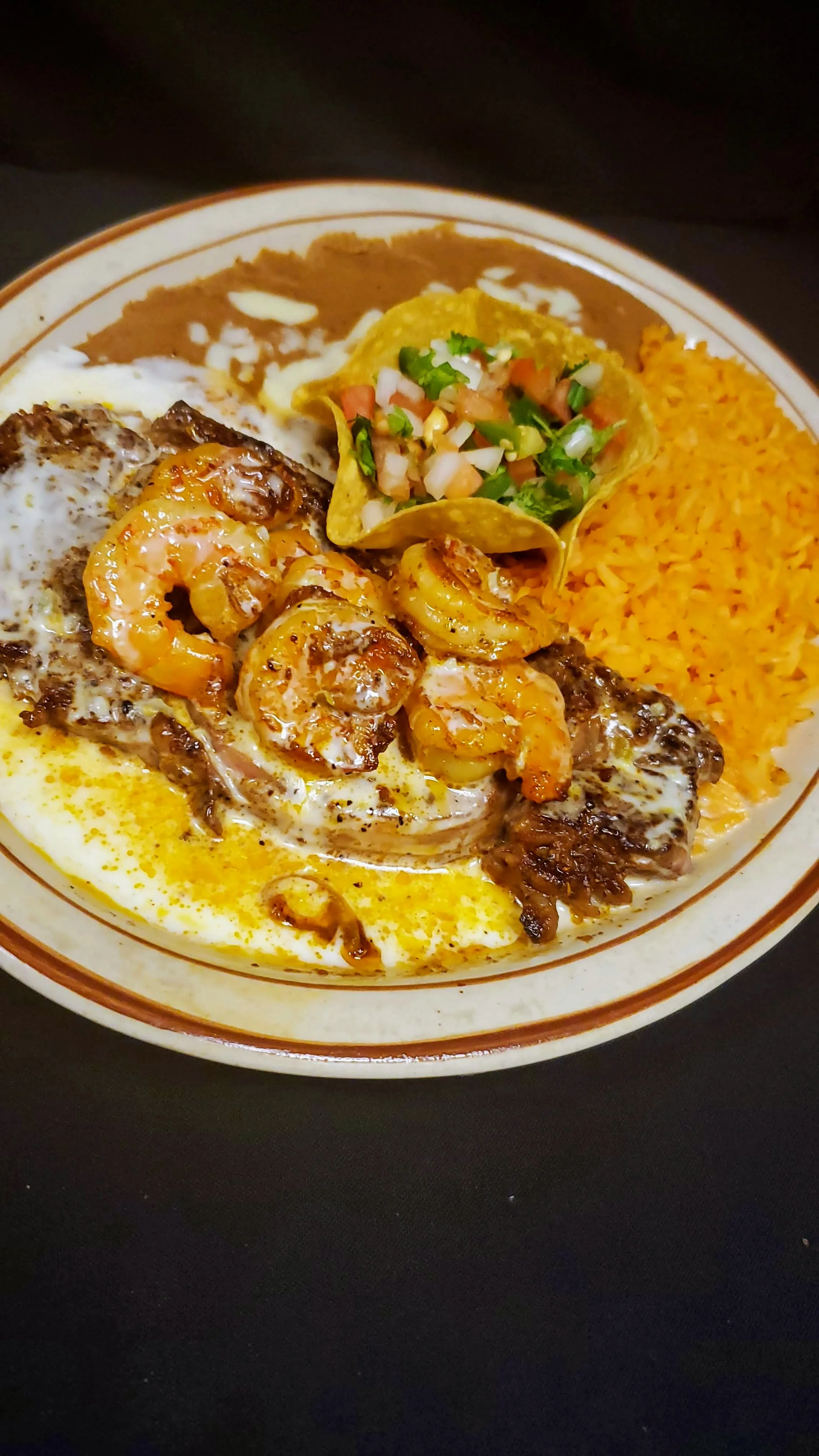 Grilled ribeye steak paired with juicy shrimp and topped with creamy queso sauce. Served with Mexican rice and refried beans. A hearty and flavorful meal with a touch of seafood and creamy richness. Best Ribeye in Radford.