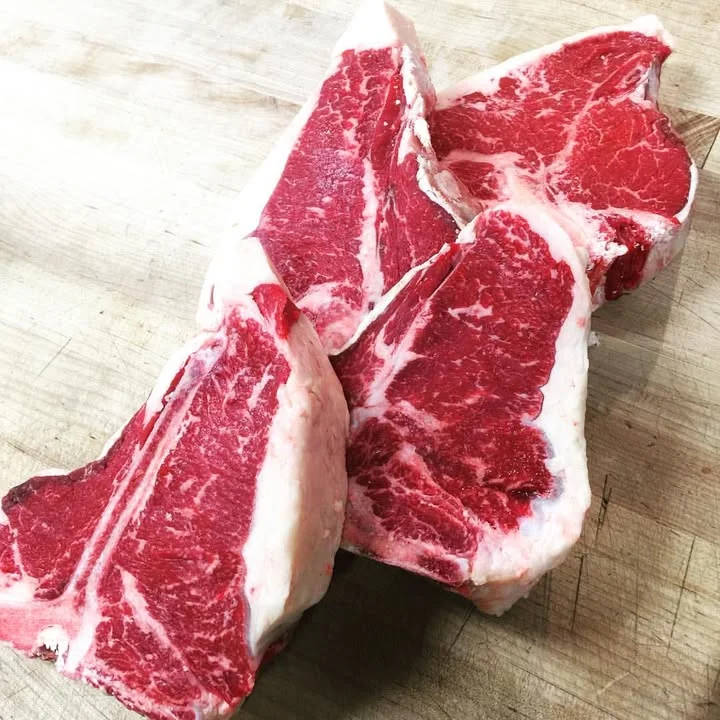 Several raw cuts of ribeye steak displayed on a wooden surface, showcasing marbling and texture.