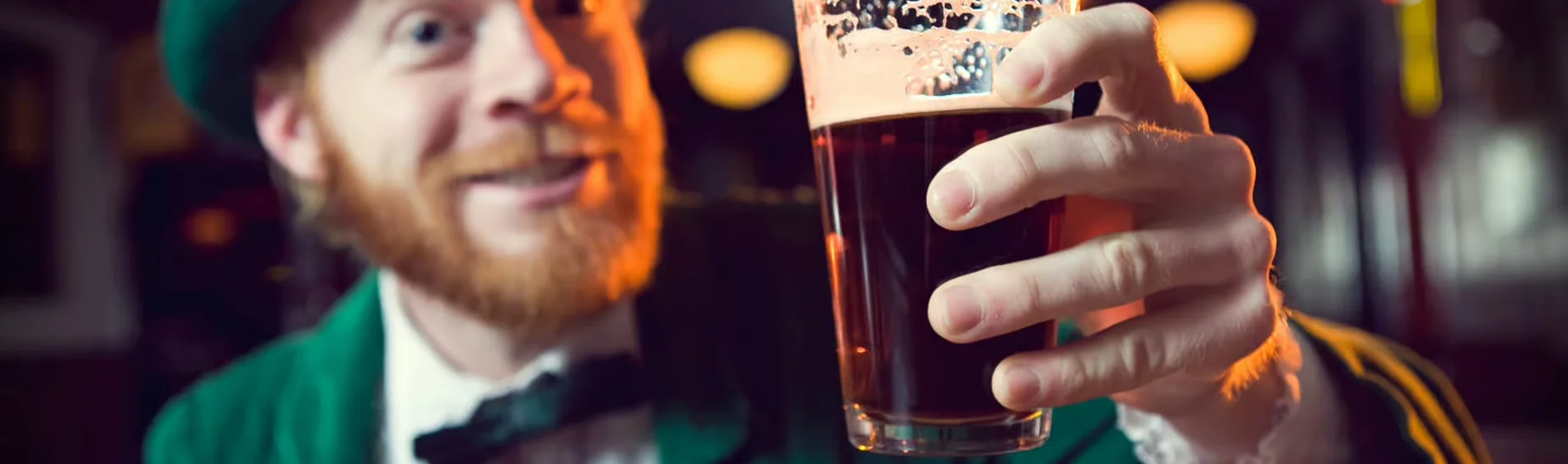 A cheerful individual in a green outfit holds up a pint of dark beer, showcasing a festive atmosphere.