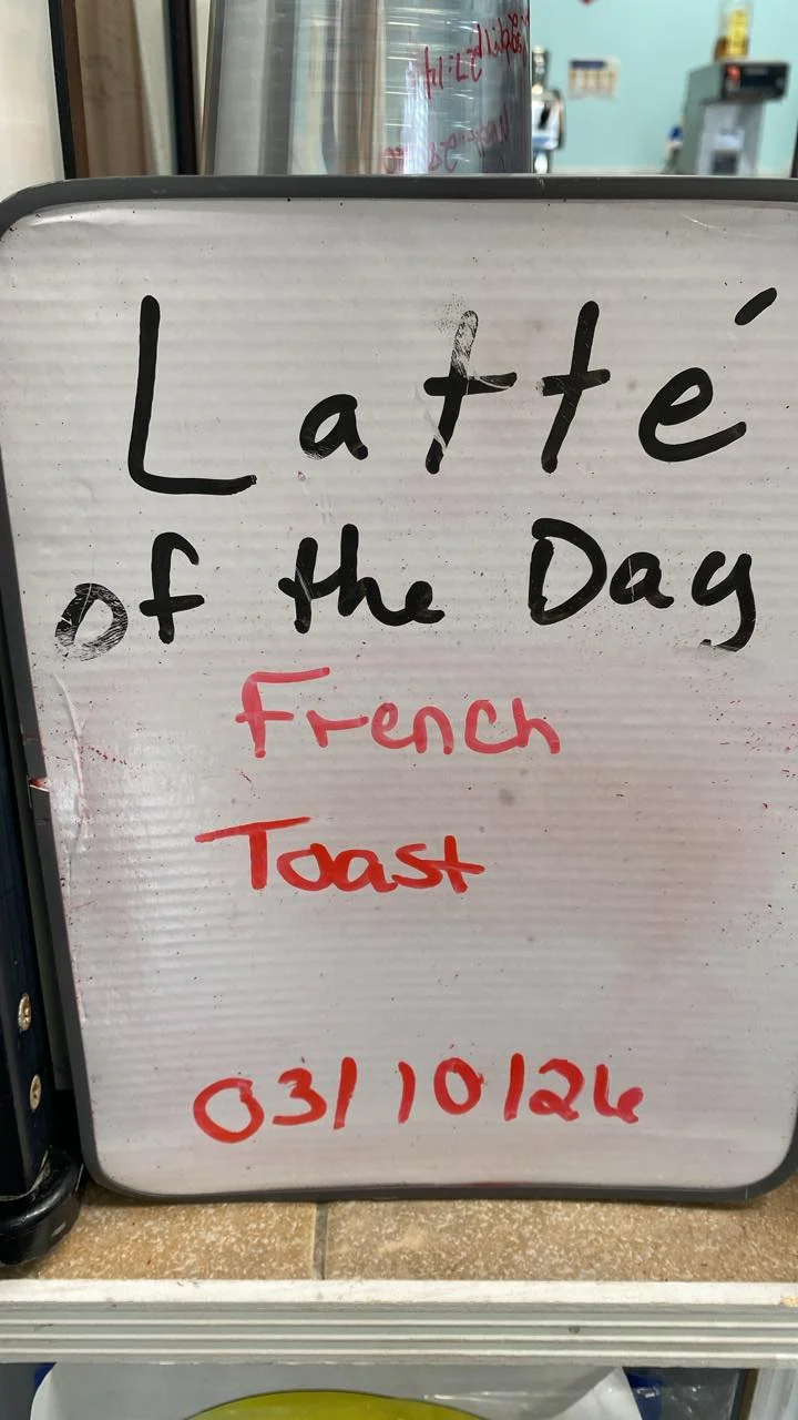 A whiteboard sign inside a cafe announcing the latte of the day as French Toast.