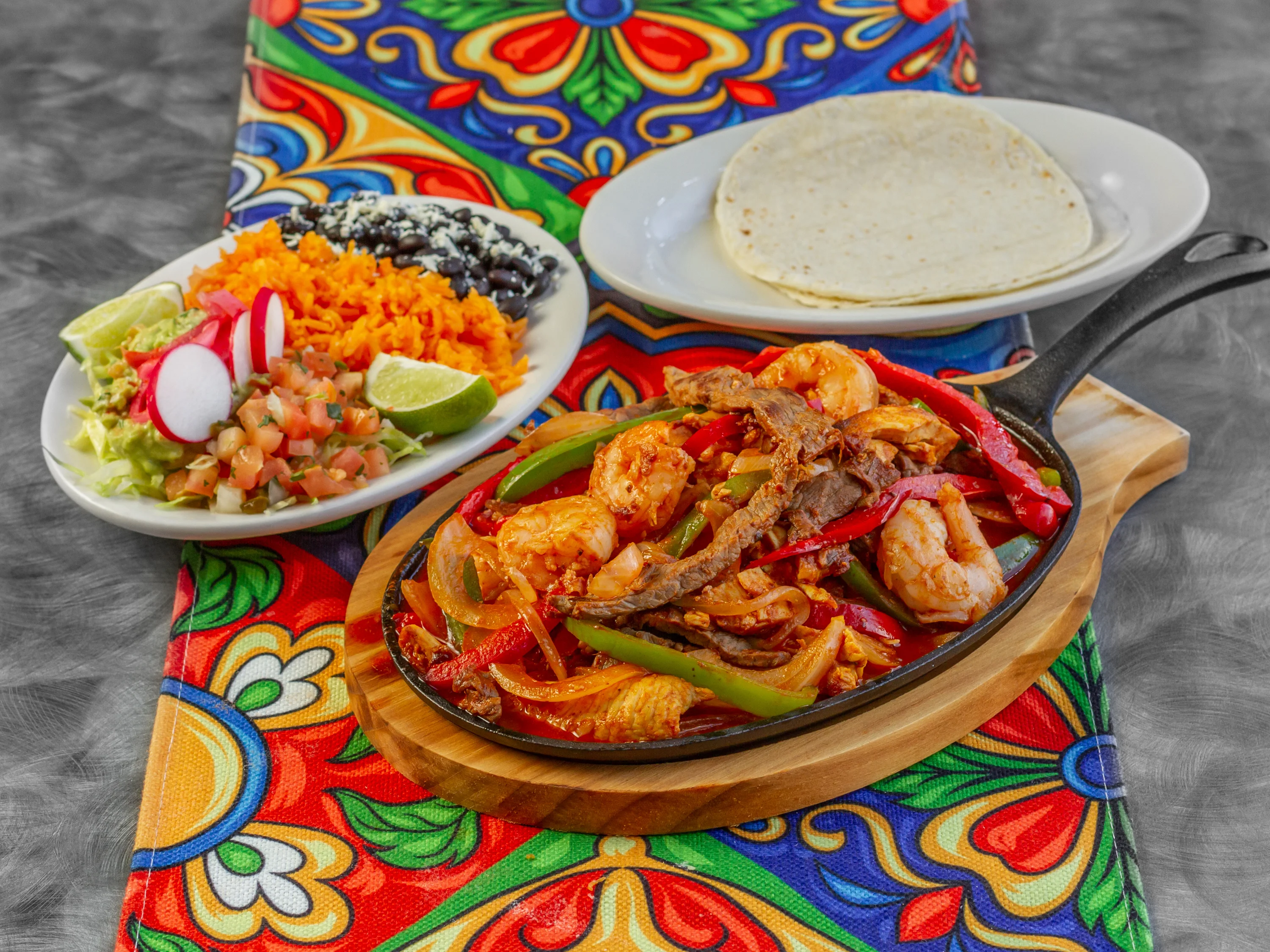 A vibrant bowl filled with rice, black beans, grilled chicken, fresh vegetables, and guacamole, presented on a colorful mat.
