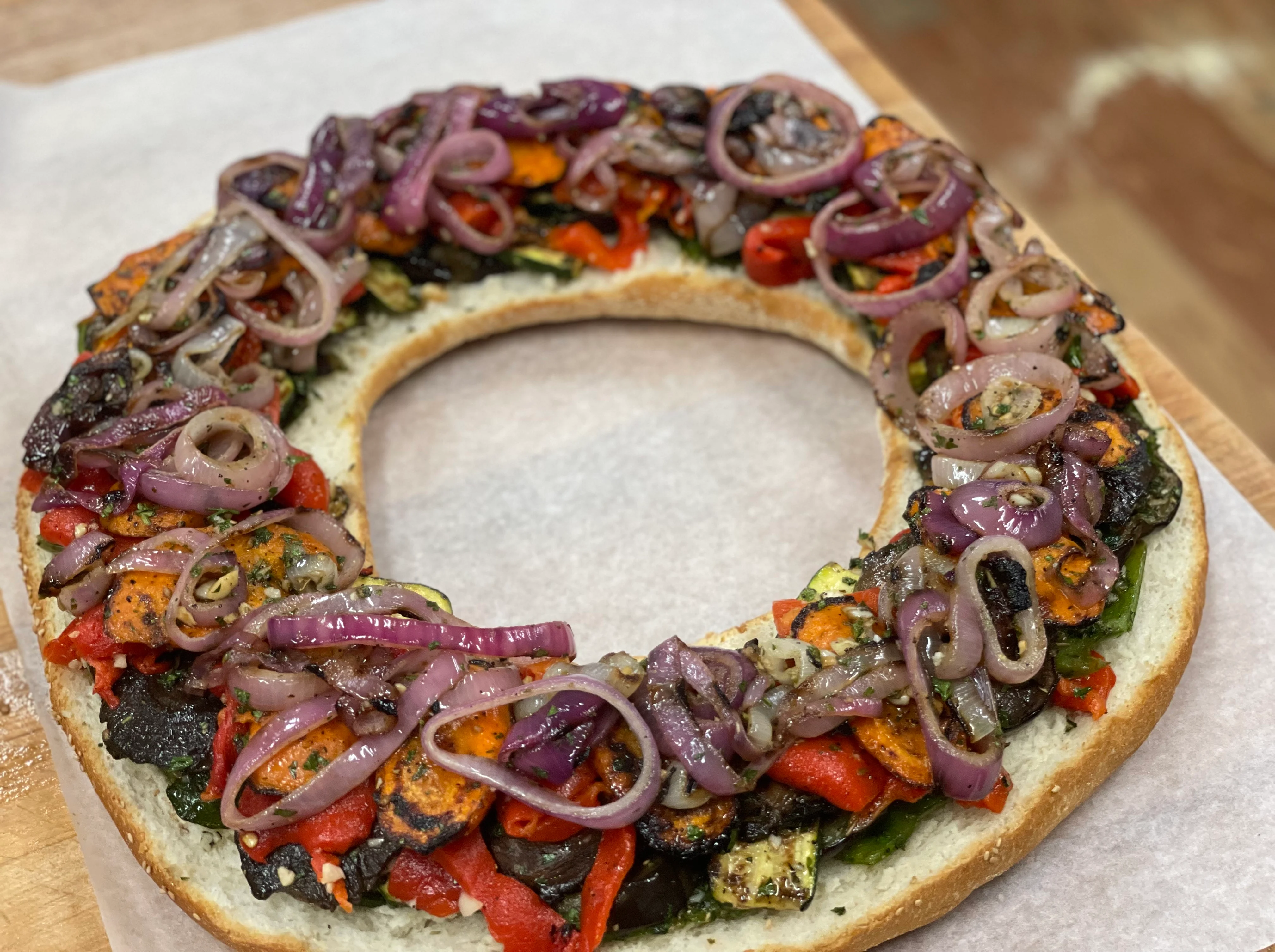 A circular bread topped with colorful roasted vegetables and onions.