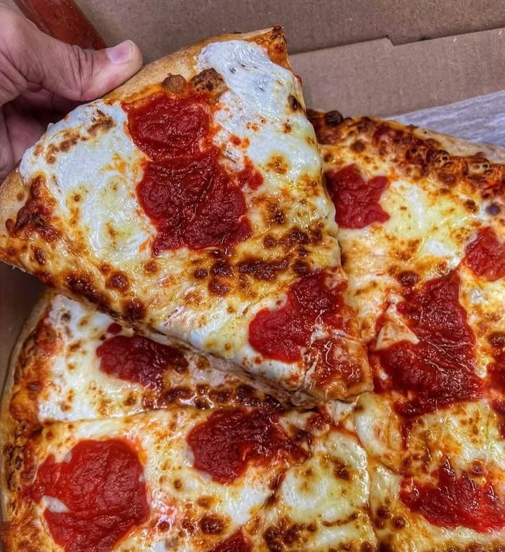 A slice of cheese pizza being held above the rest of the pizza in a box. The pizza is topped with tomato sauce and melted cheese.