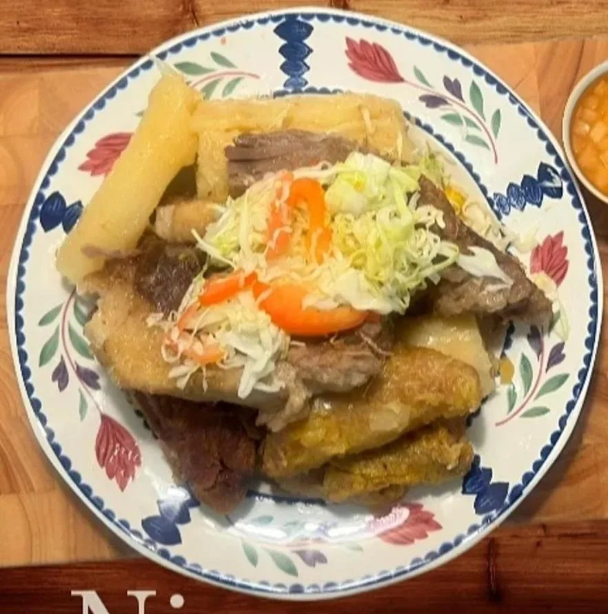 A dish of assorted meats served with boiled yuca and topped with shredded cabbage and peppers.