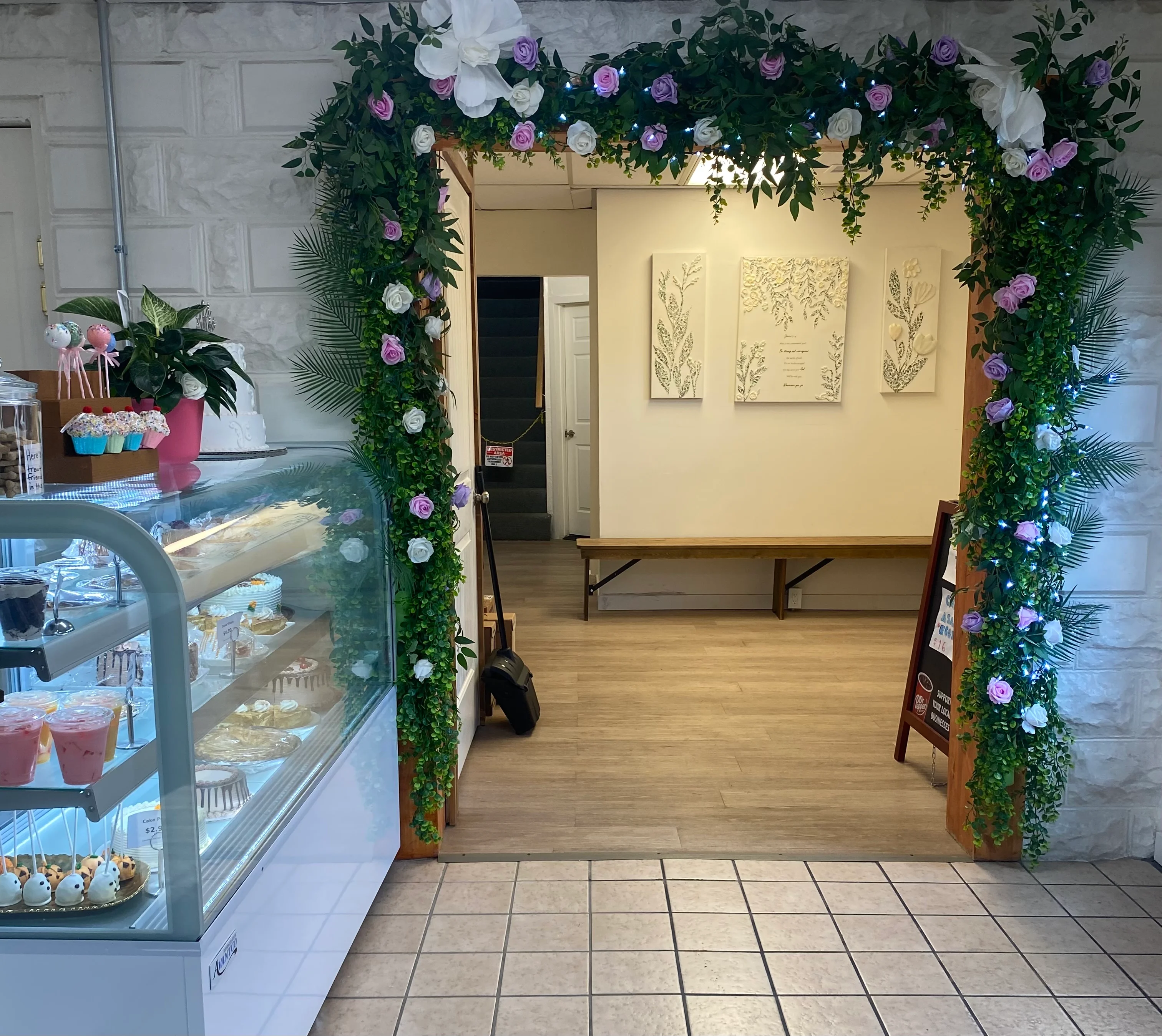 Bakery interior with floral arch, dessert display case, and decorated cakes