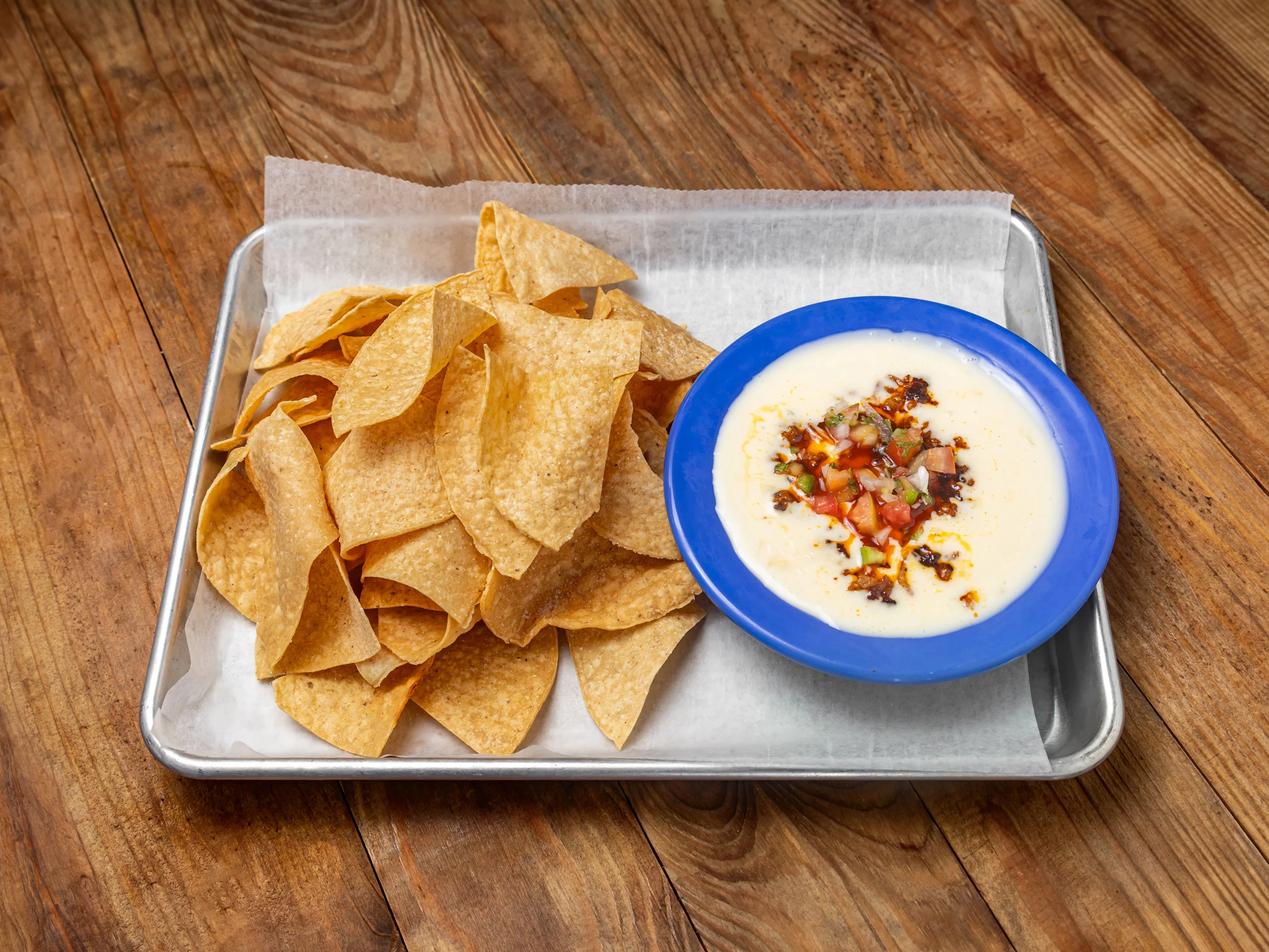 A serving of crispy tortilla chips paired with a bowl of creamy cheese dip topped with diced tomatoes.