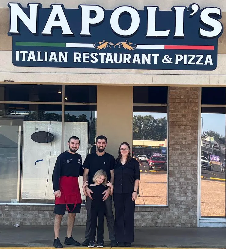 Italian restaurant storefront with team posing beneath Napoli's sign