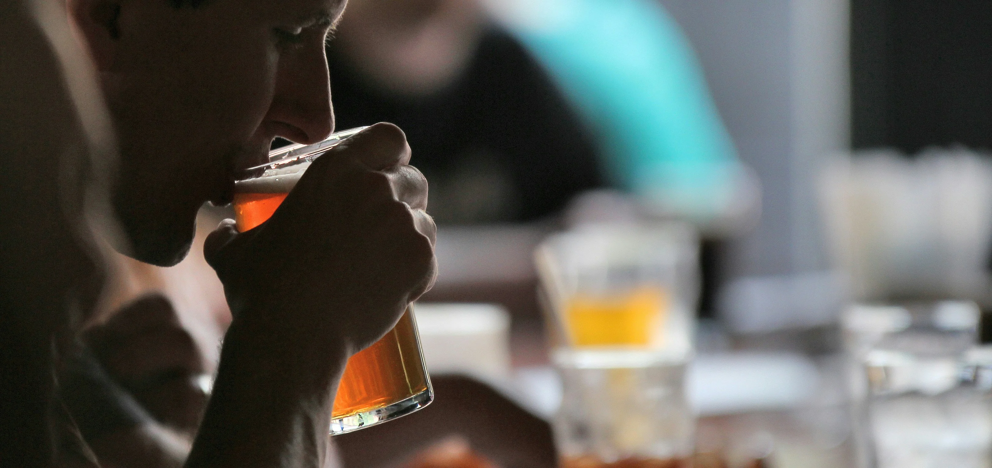 A close-up view of a person sipping a glass of amber-colored drink in a social setting.