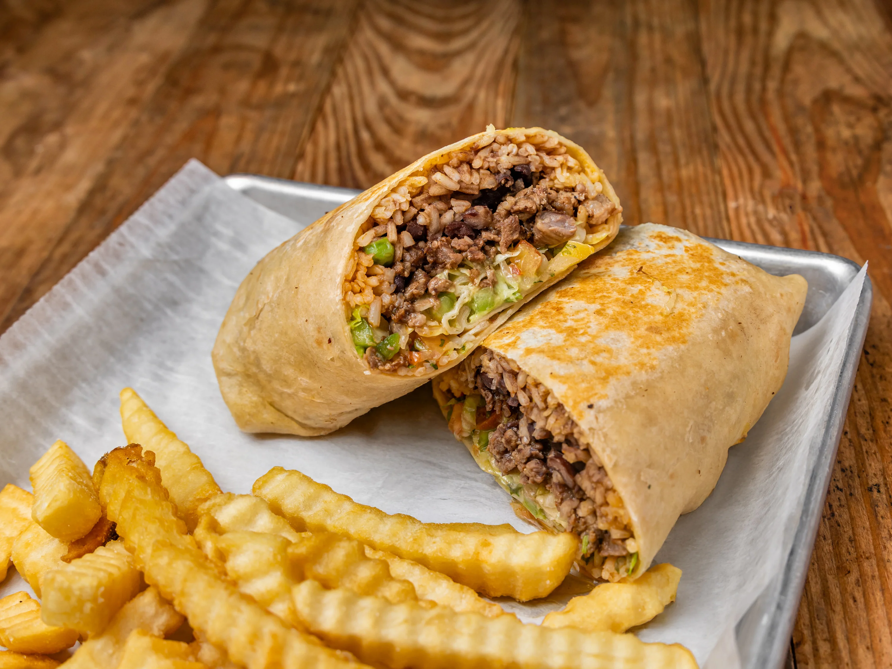 A burrito cut in half to reveal a filling of rice, beans, and veggies, accompanied by crinkle-cut fries.
