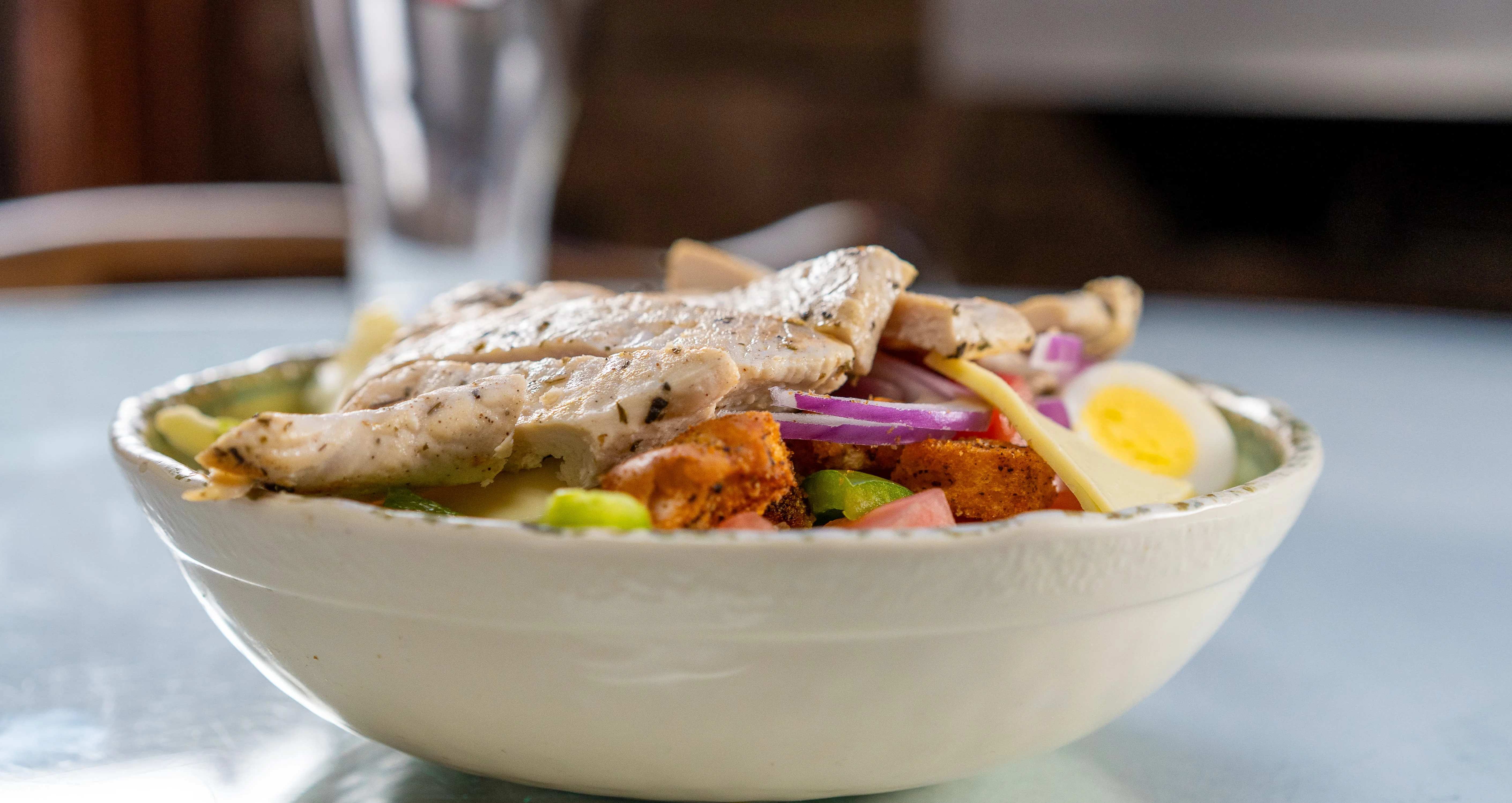 – Bowl of salad topped with grilled chicken breast, sliced boiled egg, red onion, and vegetables.