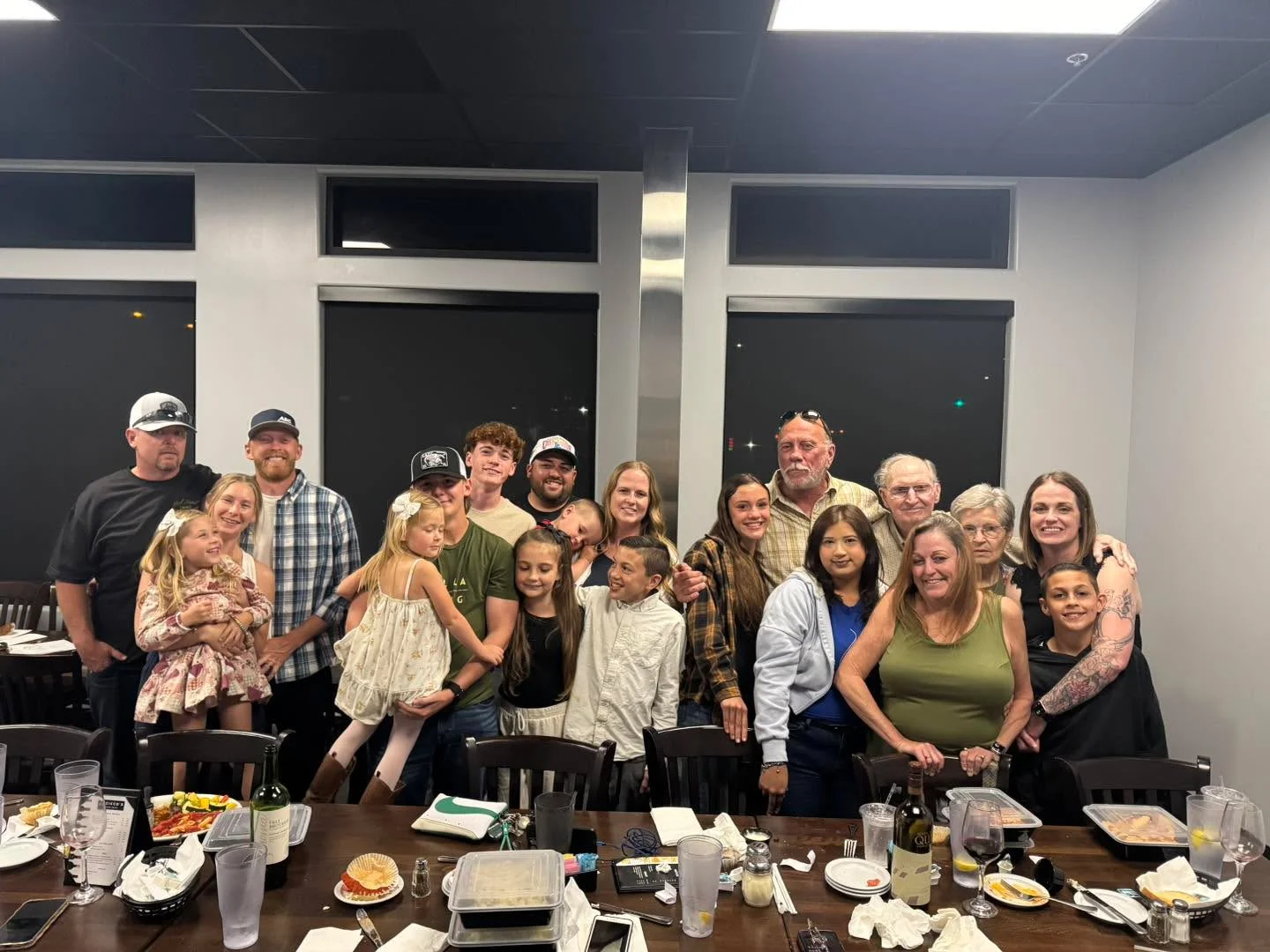 A large group of people gathered together in a restaurant, smiling and posing for the camera. The table is covered with various food items.