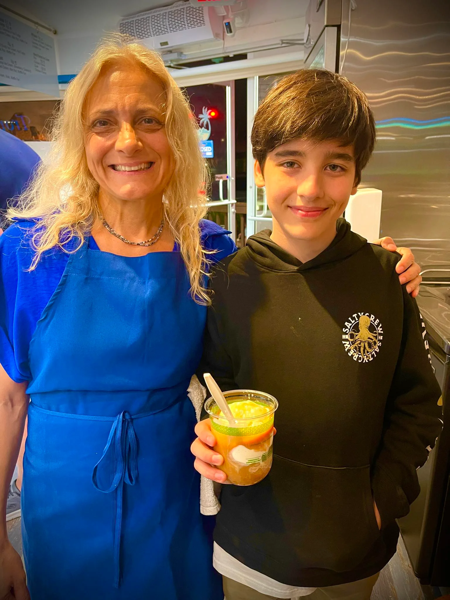 Two smiling individuals in a restaurant holding a dessert cup