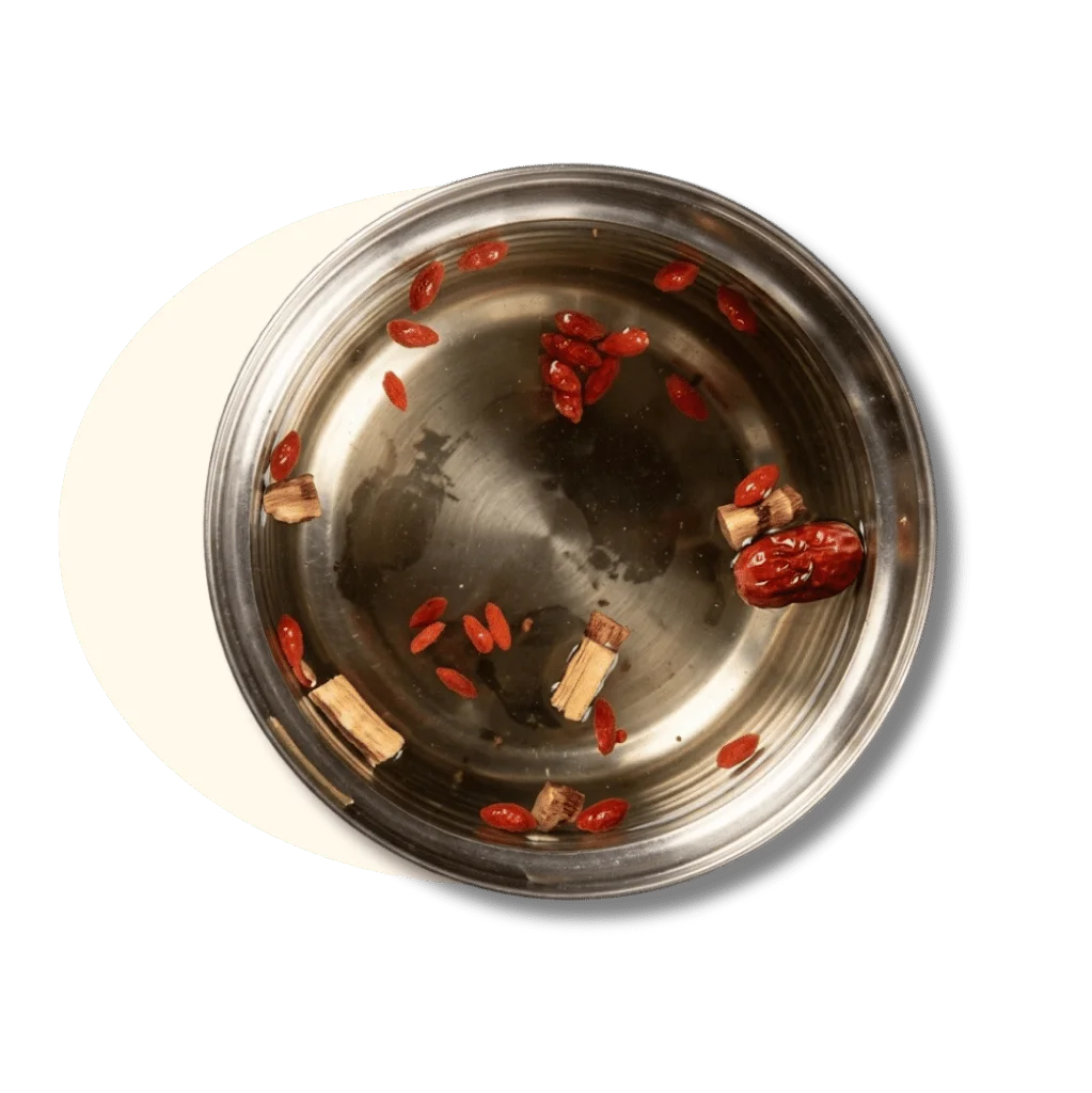 A stainless steel bowl with goji berries and herbal ingredients in water.