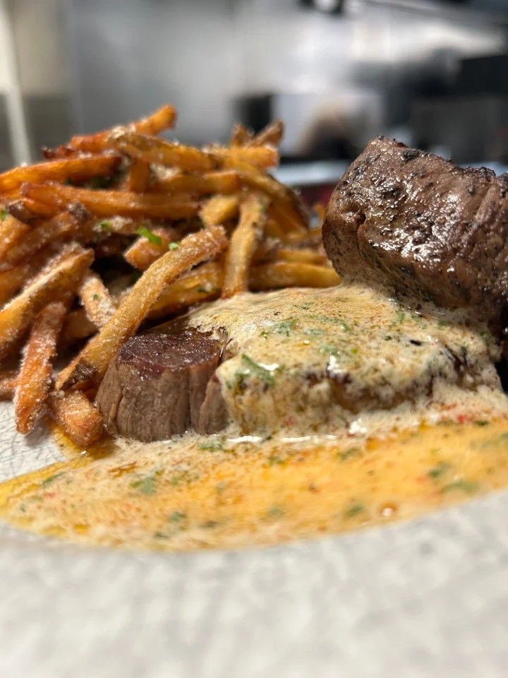 A gourmet dish of tender beef medallions accompanied by crispy fries, drizzled with a rich sauce.