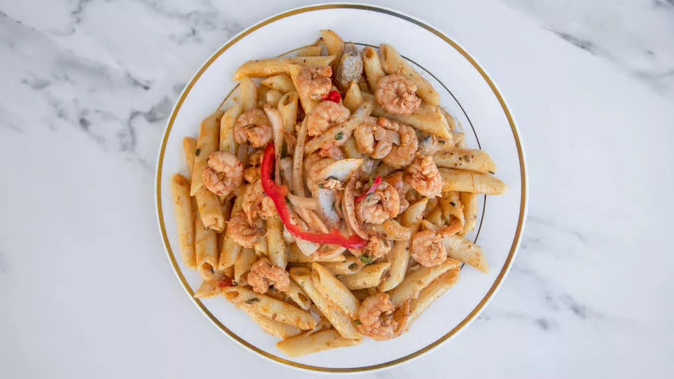 A plate of penne pasta tossed with shrimp and bell peppers in a light sauce, garnished with herbs.