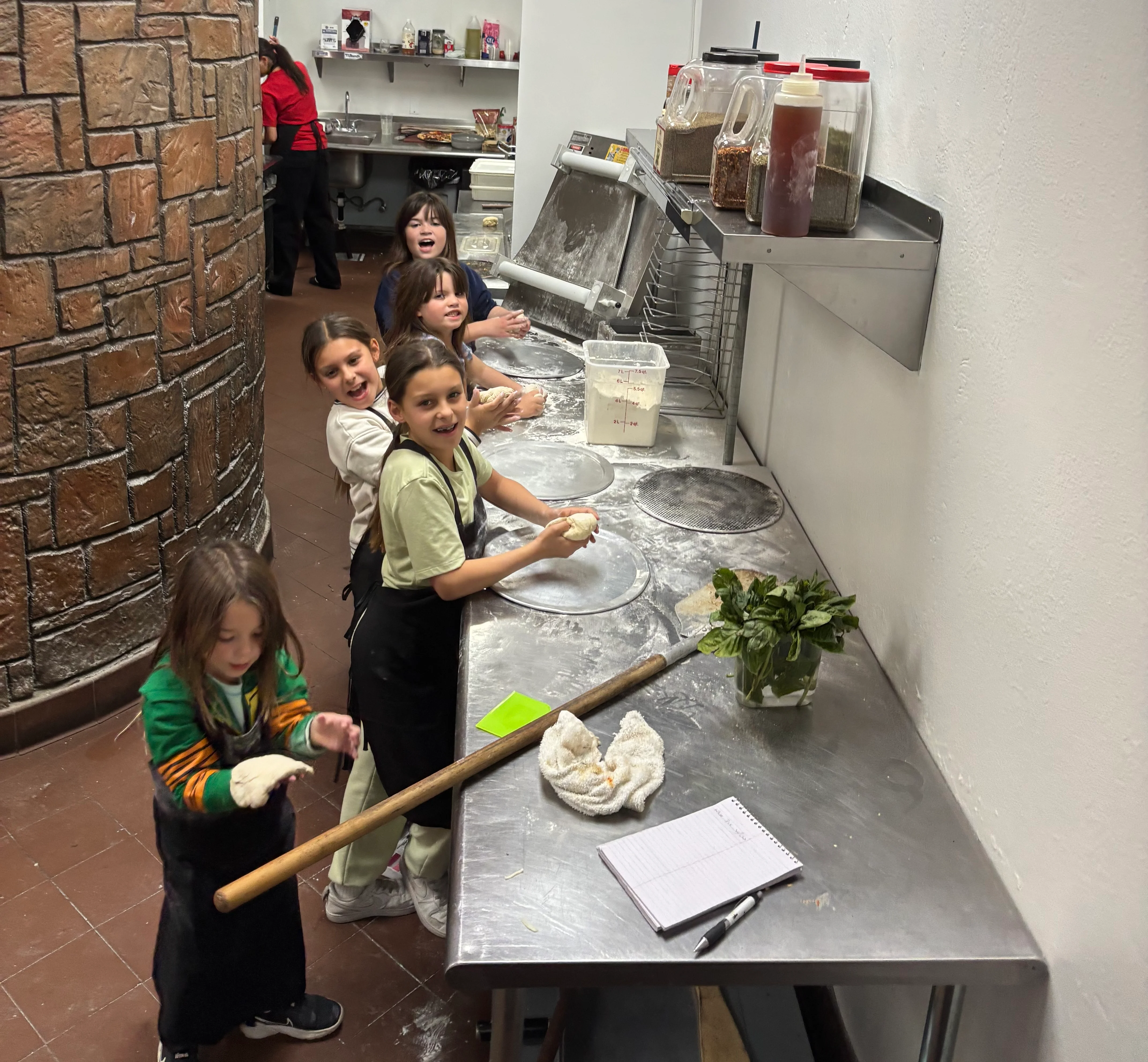 Children learning to make pizza dough in a restaurant kitchen