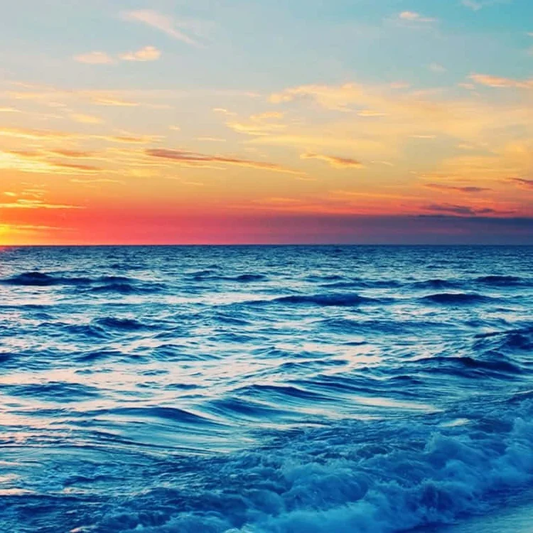Vibrant sunset over the ocean with waves lapping the shore