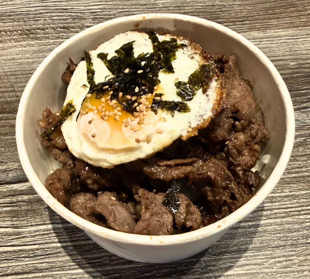 Bowl of beef with a fried egg, sesame seeds, and seaweed garnish.