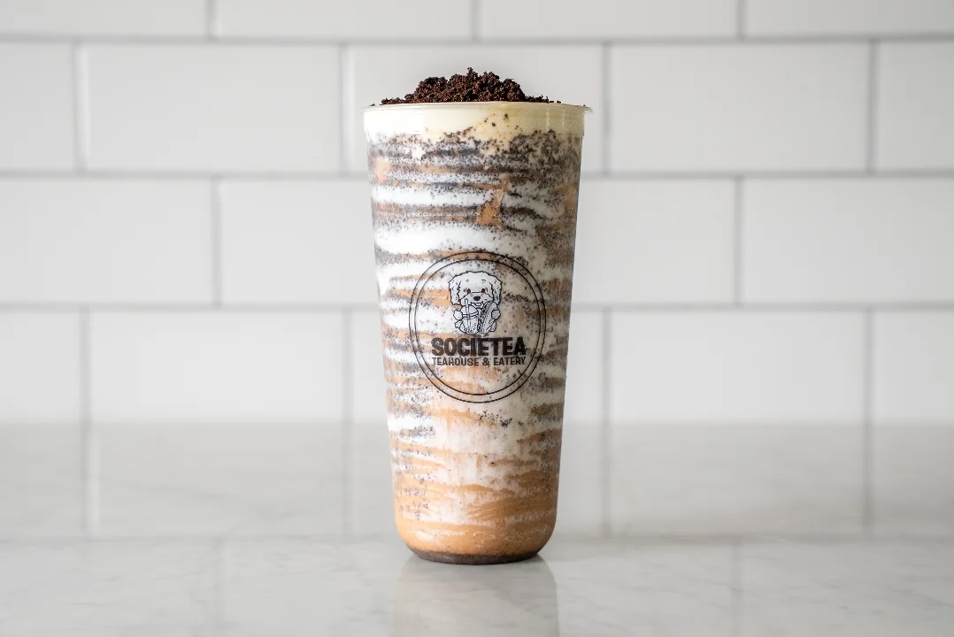 A layered beverage with a creamy and chocolatey appearance served in a transparent cup, topped with crushed cookies.