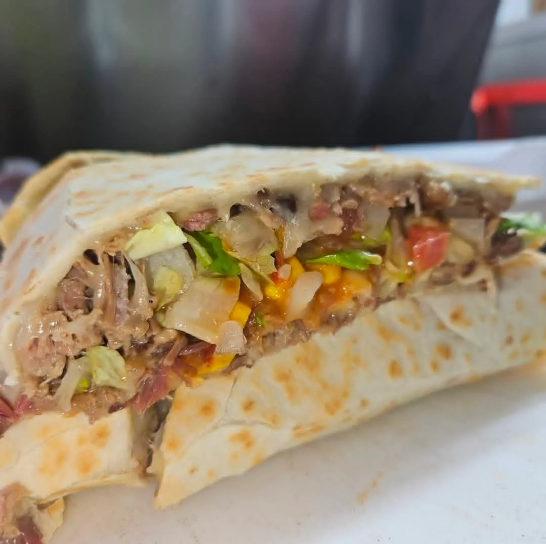 A cross-section of a large burrito filled with various ingredients, including meat, lettuce, tomatoes, and cheese, wrapped in a grilled tortilla.