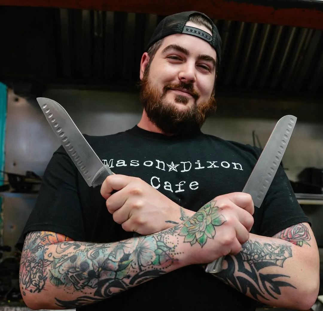 Chef posing with knives in a vibrant kitchen