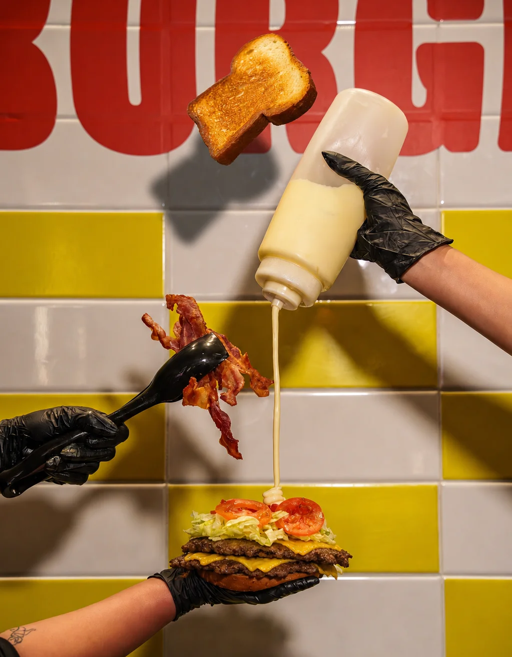 Classic American burger being assembled with bacon and mayonnaise