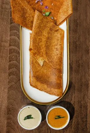 A plate of crispy dosa served with two types of chutneys on the side.