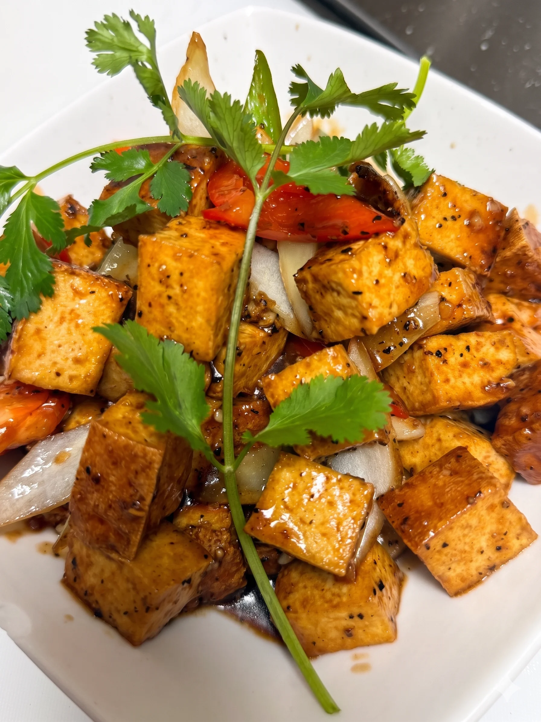 Stir-fried tofu with vegetables and cilantro in a white bowl.