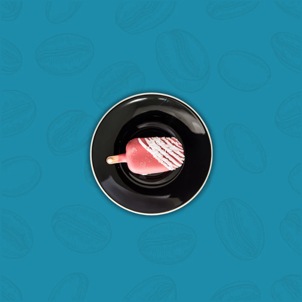 A pink ice cream popsicle with white drizzle on a black plate against a textured teal background, creating a fresh and vibrant feel.