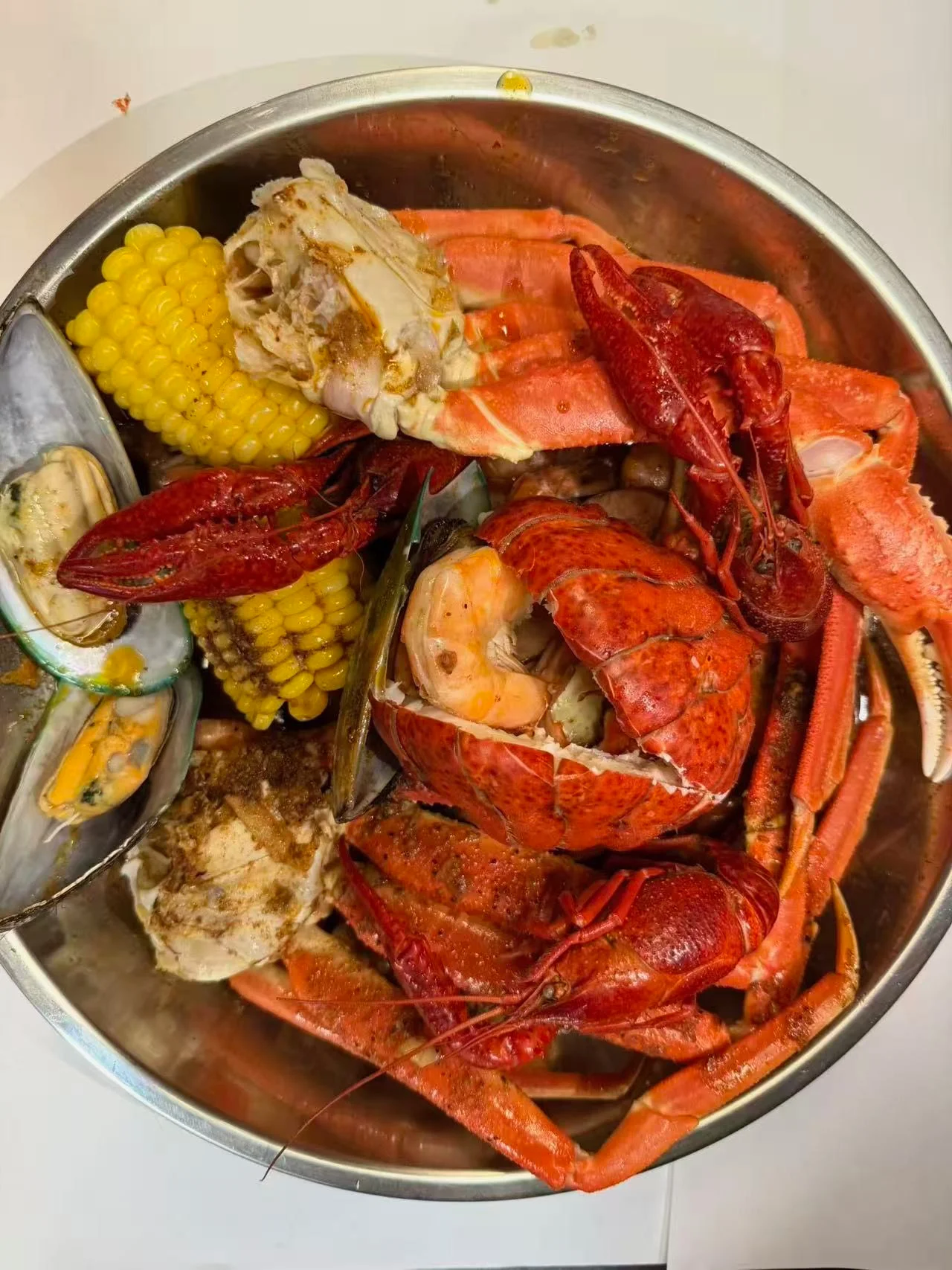 A large metal bowl filled with a variety of seafood, including lobster, crab, shrimp, and corn on the cob, arranged attractively.