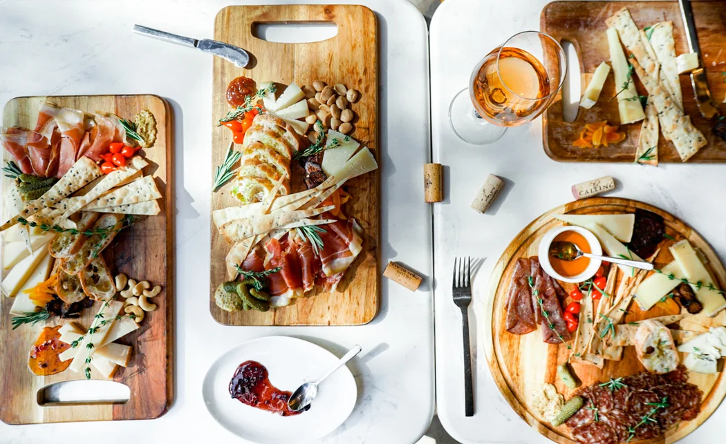 An assortment of charcuterie and cheese platters featuring meats, cheeses, nuts, and garnishes. The display includes a variety of textures and colors, arranged beautifully on wooden boards.