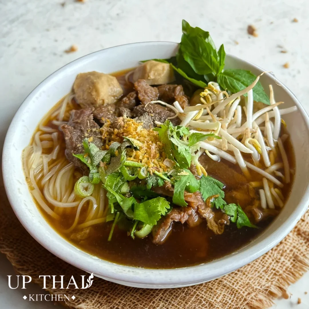 Bowl of Thai boat noodles with fresh herbs and beef