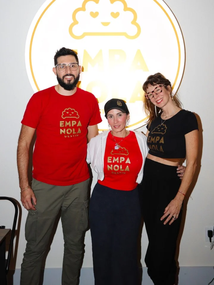 Three people in matching apparel pose in front of a logo, exuding a friendly atmosphere in a dining space.