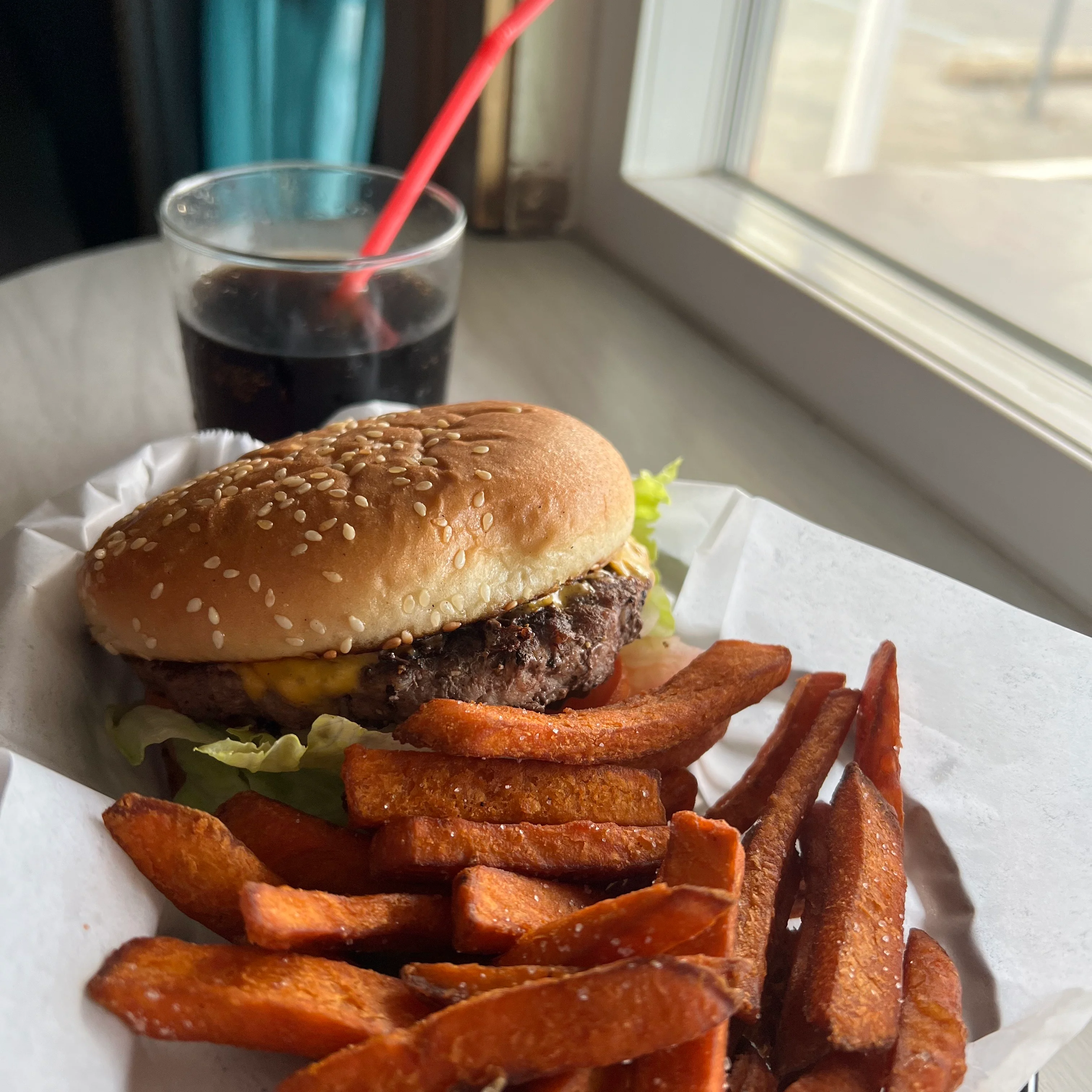 Juicy bacon cheeseburger from Countryside Drive-In, loaded with melted cheddar cheese, crispy bacon, fresh lettuce, ripe tomatoes, pickles, and onions on a toasted sesame-seeded bun. Paired with golden fries and a cold drink, perfect for a classic burger experience.