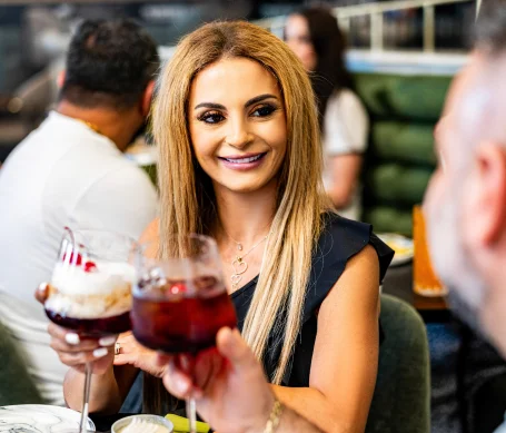 Smiling woman toasting with cocktails in a vibrant restaurant setting